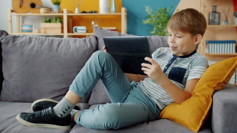 Kind liegt auf Sofa mit Tablet